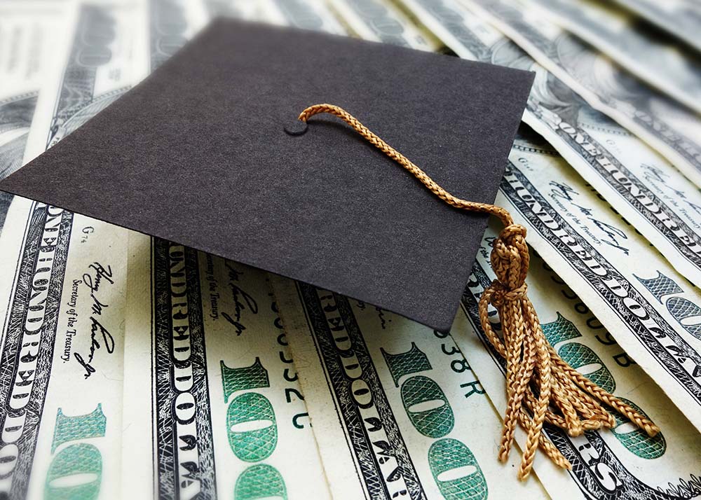 Mini graduation mortar board cap on money -- education cost or scholarship concept
